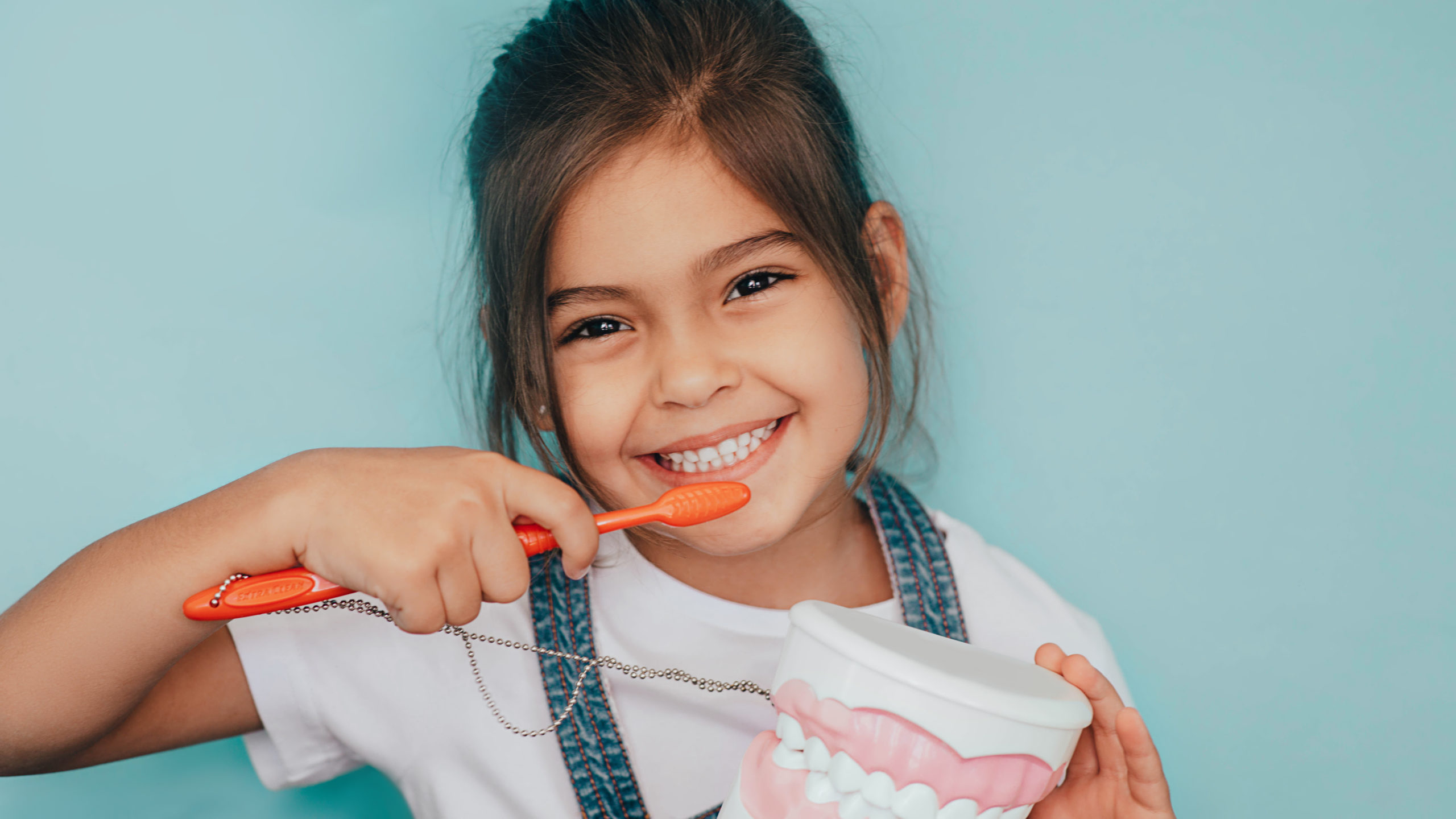 smiling mixed raced girl brushing teeth at blue background.